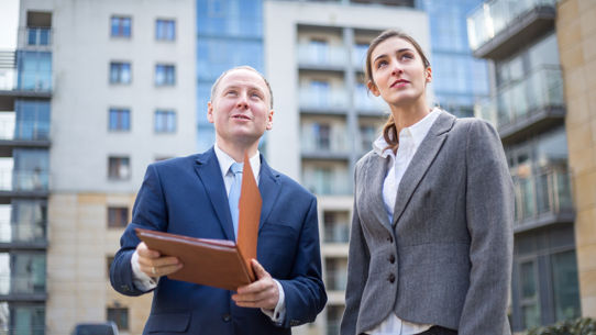 A man holding a clipboard with a woman surrounded by apartment buildings