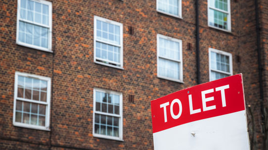 A 'To Let' sign in front of a brown apartment complex