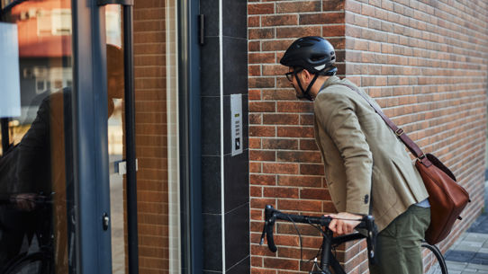 A man on a bicycle looking at a comms system outside a building