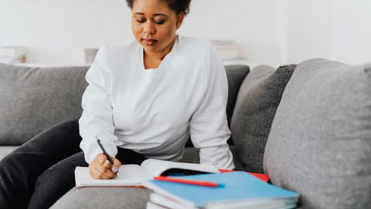 A woman writing in a notepad on a sofa